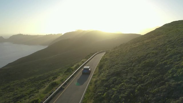 Car driving along the winding coastal roads of the Marin Headlands in San Fransisco, California, at sunset. Aerial follow shot