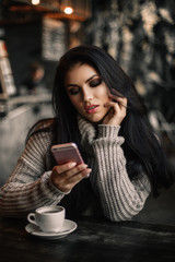 Woman using phone and drinking coffee in a cafe.