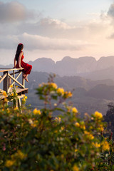Rear view of a female tourist in a red dress sitting and watching the beautiful scenery during sunrise of Doi Tapang (Doi Ta Pang) Viewpoint at Chumphon province in Thailand.