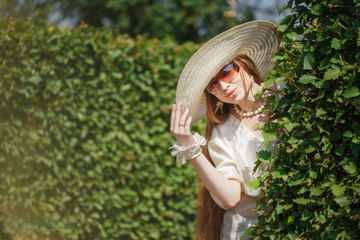 Beautiful emotional girl in a hat walks in a vintage park. Fashionable woman in retro style. Romantic model with long hair