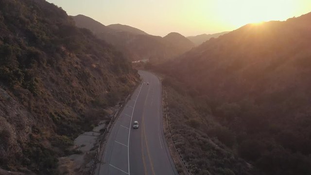 Aerial Slow Pan Up View of Cars Driving Down Street Slowly Between Beautiful California Mountains and Hills During Gorgeous Sunset Bright Orange Sunny Sky in Burbank Los Angeles California 4K Drone 