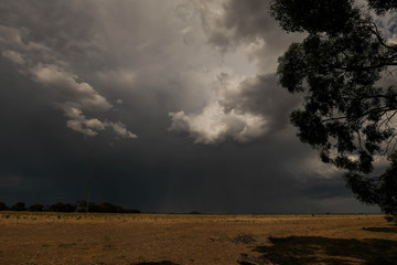 Storm clouds creating stormy sky over dry paddocks during times of drought in Central Victoria,...