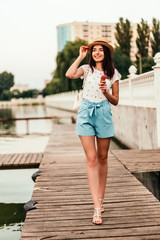 Beautiful young woman walking with ice cream on pier at sunset in summer.