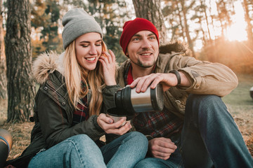 Travel couple camping with thermos having fun in the forest. Concept of trekking, adventure and seasonal vacation.