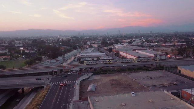 Aerial View in Culver City California During Sunset with Cotton Candy Sky Overlooking Hollywood Hills Skyline Mountains and Metro Train Passes with Cars at Intersection Evening Night Sunset 4K Drone