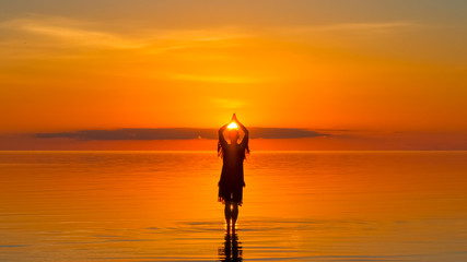 Girl at sunset worshiping the sun, cheerful religion, seascape, trend color Lush Lava