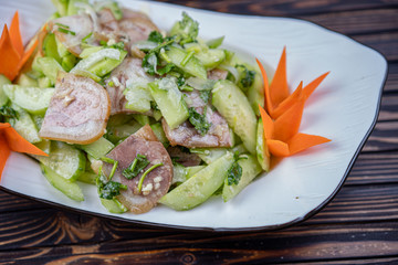 Typical Chinese salad of cucumbers and pork in a white plate on a wooden background