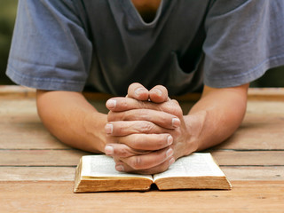Praying hands of middle aged man on old wooden desk.