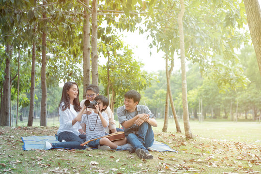 Asian father use digital camera take group photo of his wife,son and grandma in public park,Happy together of asia family have leisure activity in weekend.