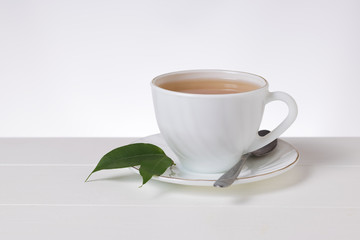 Tea in a white porcelain Cup and a metal spoon on a white table.