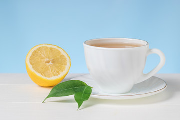 A Cup of tea with half a lemon on a white table on a blue background.