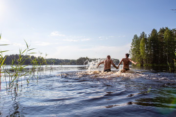 Man and a woman hold hands, swim and have fun in a clear forest lake on a hot summer day. Active tourist life.