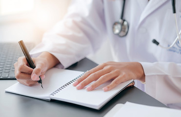 Fototapeta premium Cropped shot of female doctor writing recipe on notebook while working at office desk in hospital.