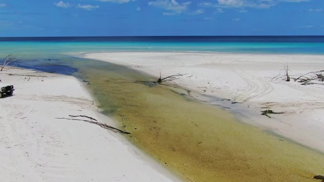 Stunning aerial drone footage of a white coloured four-wheel drive off-road vehicle crossing Awinya Creek on the west coast of Fraser Island, Queensland, Australia. Water is splashing, the car shaking