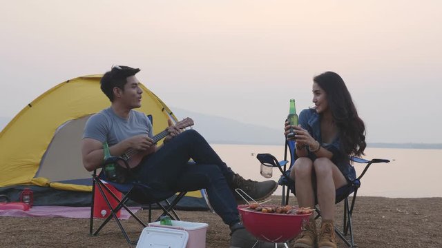 Young asian couple at camping site ,man playing ukulele and woman listening and sing a song.