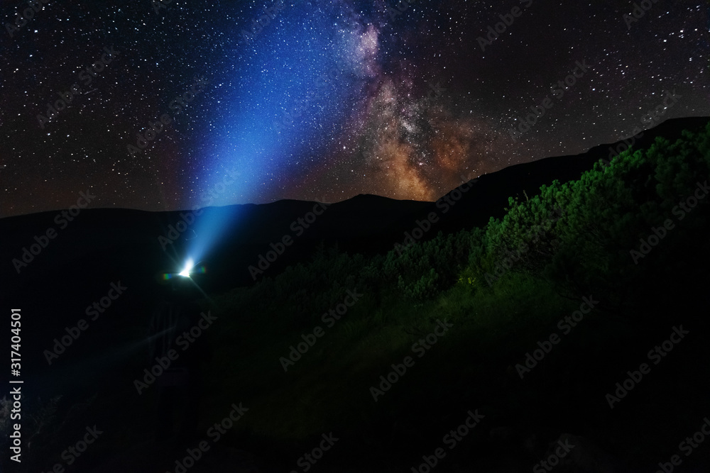 Wall mural bright starry sky with the milky way on the background of mountains and hiker with red tent.