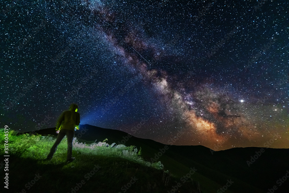 Wall mural bright starry sky with the milky way on the background of mountains and hiker with red tent.