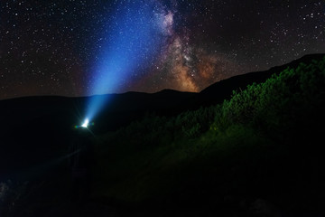 Bright starry sky with the milky way on the background of mountains and hiker with red tent.