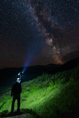 Obraz premium Bright starry sky with the milky way on the background of mountains and hiker with red tent.