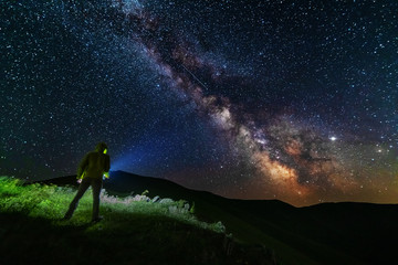 Bright starry sky with the milky way on the background of mountains and hiker with red tent.
