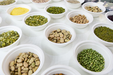 Peeled beans in a white plastic plate. Around in the same plates are various seeds, nuts and beans.