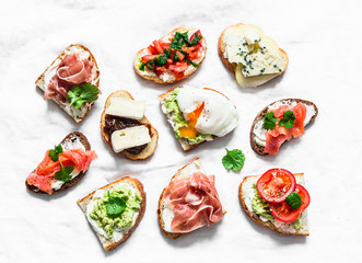 Variety of tapas sandwiches  - sandwiches with prosciutto, avocado, salmon, egg, tomatoes, jamon, gorgonzola, brie, pear on a light background, top view. Delicious snack, appetizers