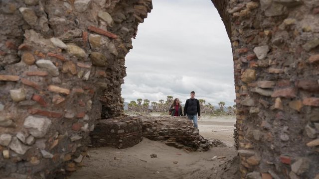 Lovers holding hand go into the ruined arch of ancient Torre Flavia in Ladispoli, Rome, Italy