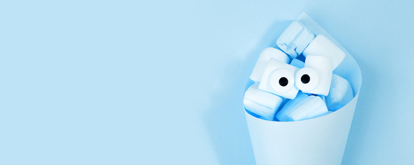 Marshmallows with eyes in paper cone. Funny kawaii emoji face. Cute cartoon character. Minimal summer flat lay design. Sweet food. blue background, monochrome, banner