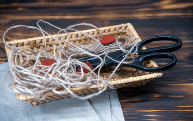 A wicker basket with scissors, coarse thread, and red felt hearts stands on Kraft paper