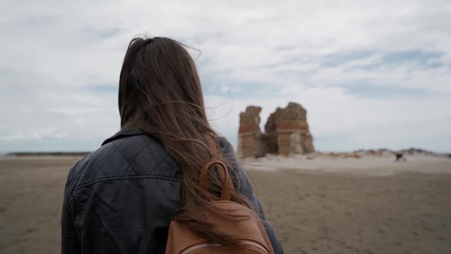 Tourist girl with a backpack approaches the ruins of an ancient fortress Torre Flavia in Ladispoli, Italy. Rear view