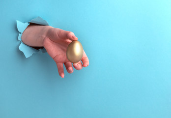 Golden egg in a female hand on a blue background with a hole, profit concept