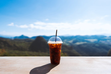 Ice americano up on the wood table at sky cafe. Natural mountain valley view point relax and refresh from travel. Background with copy space. Ja bo, Mae Hong Son, Thailand.
