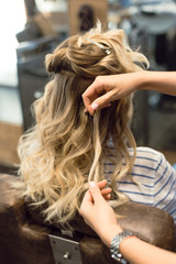Fototapeta premium The hairdresser creates curls and wavy hair in the blonde. Hands of the hairdresser curls curls at the client