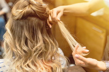 The hairdresser creates curls and wavy hair in the blonde. Hands of the hairdresser curls curls at the client