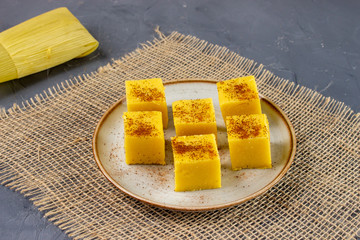 Pieces of Canjica or Curau. Tipical brazilian food made from corn. Festa Junina. In a plate on grey background.