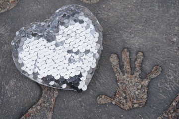 Silver heart on concrete background and trace of a child’s hand, concept of love and peace