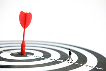 Business strategy conceptual photo - Miniature businessman walking toward red arrow at the center of dartboard