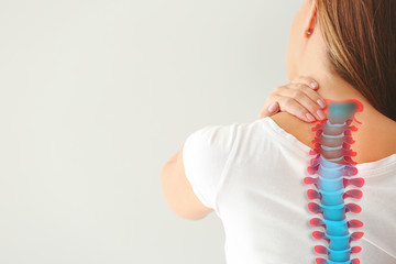 Young woman suffering from back pain on light background