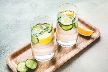 Glasses of cold cucumber water on color background