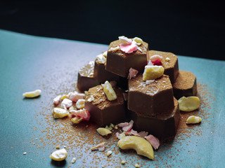  piled up chocolate with top of crushed hazelnuts, pink chocolate pieces and cocoa powder on dark background.