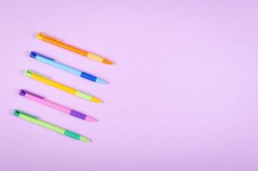 Different colored pens, school ballpoint on purple background composition.