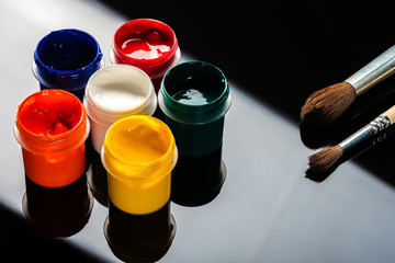 paint gouache in jars, with brushes, on a black and gray background with a reflection