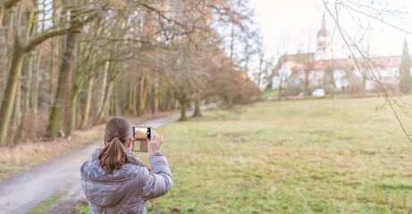 eine junge Frau macht mit dem Smartphone ein Foto vom Schloss im Schlosspark Wechselburg im Winter