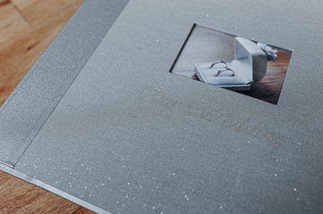 gray shine textile wedding photo album with a picture of a pair of smooth silver rings in a box and the inscription our wedding on a wooden cover