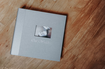 gray shine textile wedding photo album with a picture of a pair of smooth silver rings in a box and the inscription our wedding on a wooden cover