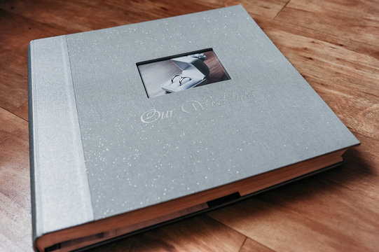 gray shine textile wedding photo album with a picture of a pair of smooth silver rings in a box and the inscription our wedding on a wooden cover