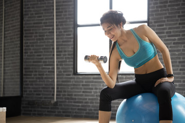 Fototapeta na wymiar Happy Young Asian Woman doing exercises with dumbbell at gym In a room with a window with natural light. Fitness and healthy lifestyle concept