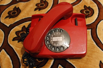 Red old Soviet dial phone with the handset removed on the background of a vintage rug