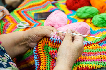 hands of an old woman with knitting needles, knitting from multi-colored yarn