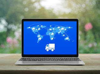 Delivery truck icon with connection line and world map on modern laptop computer screen on wooden table over blur pink flower and tree in garden, Business transportation online concept